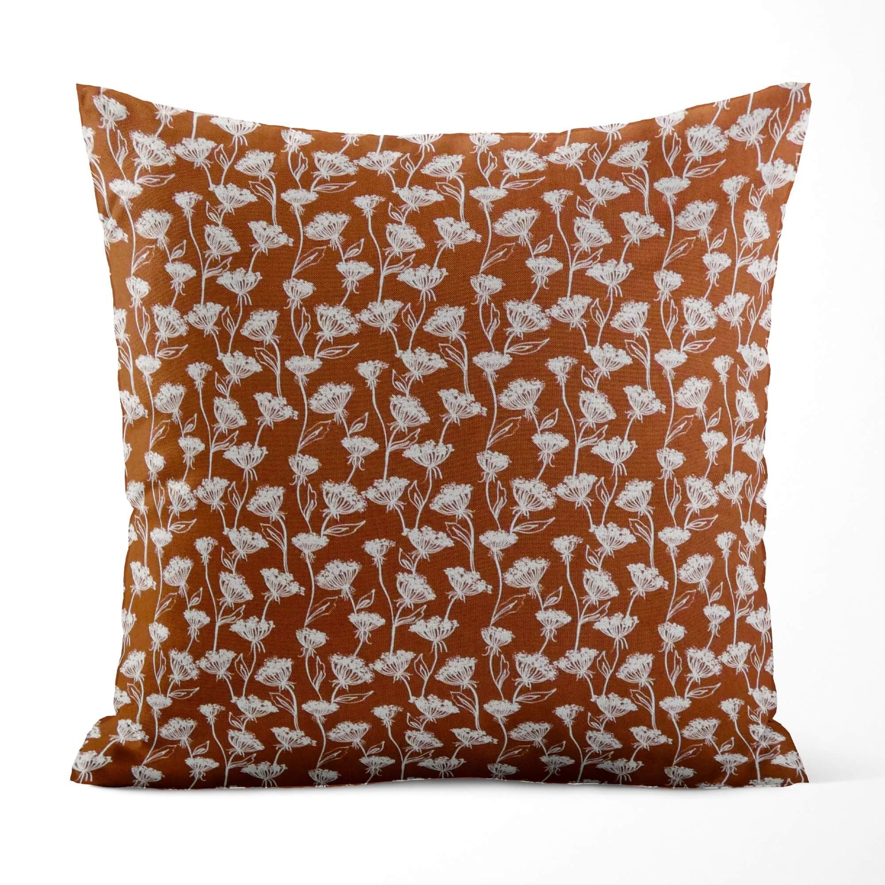 Decorative pillow with white floral pattern on a rust-colored background