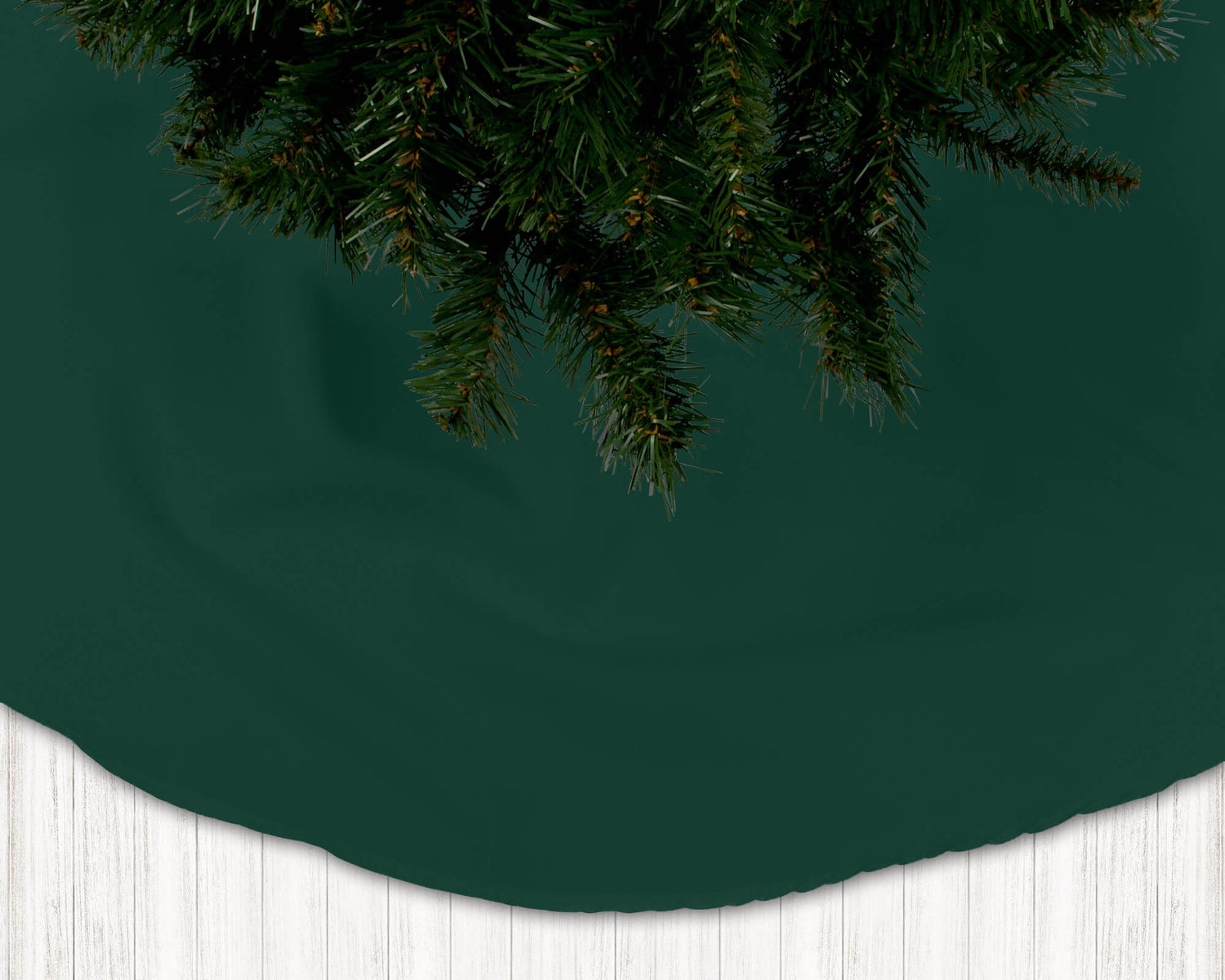 Dark green Christmas tree skirt with pine branches on a white floor.