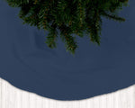 Navy blue Christmas tree skirt with green pine tree branches on a white floor.