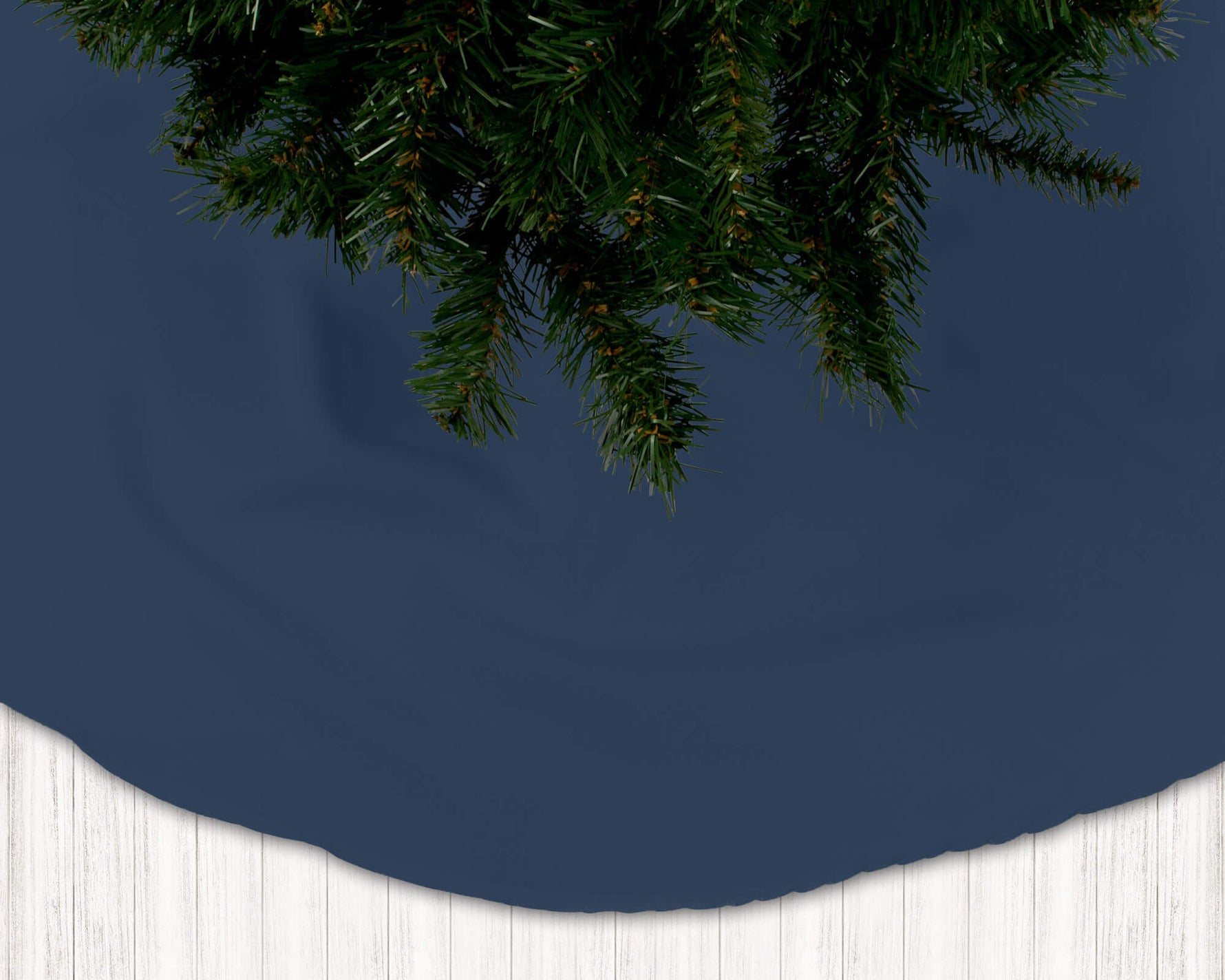Navy blue Christmas tree skirt with green pine tree branches on a white floor.