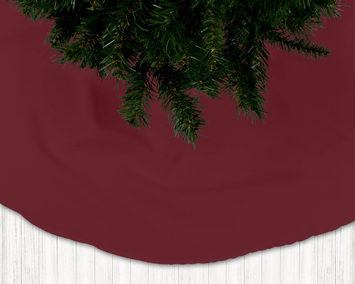 Burgundy Christmas tree skirt with a portion of a Christmas tree visible above it.