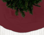 Burgundy Christmas tree skirt with a portion of a Christmas tree visible above it.