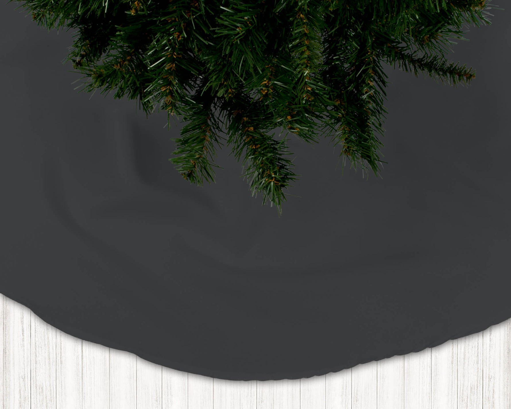 Dark gray Christmas tree skirt with a section of a decorated tree on a white floor.