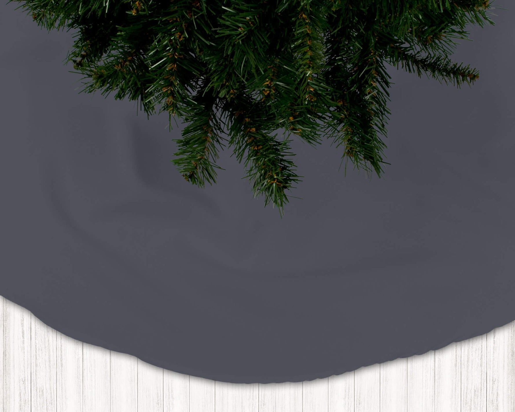 Dark gray Christmas tree skirt with green pine branches on a dark background